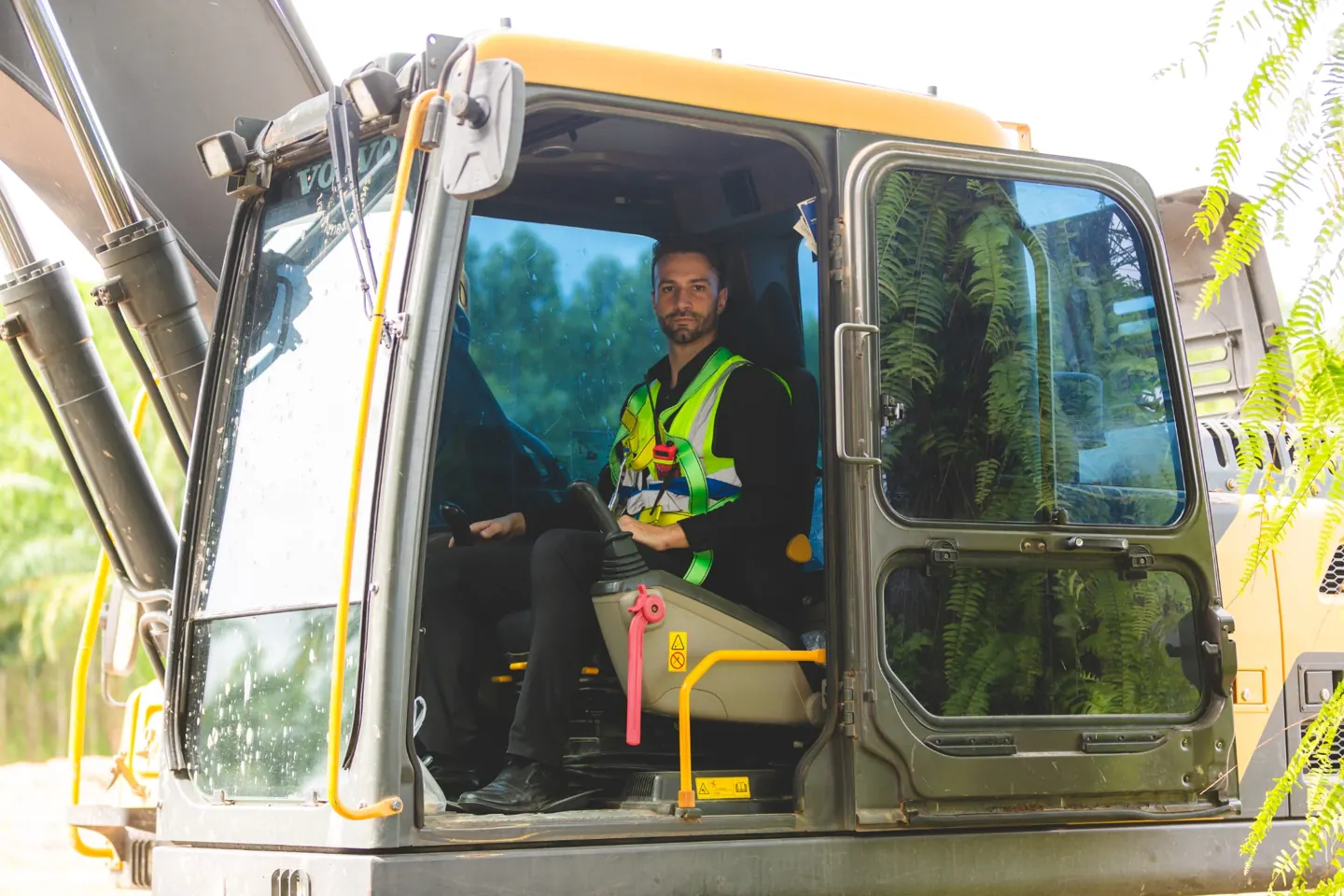 Heavy equipment operator seated inside excavator cab with large glass windows